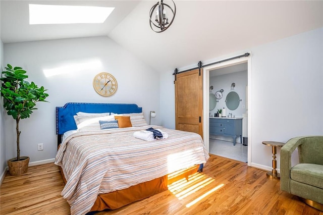 bedroom with a barn door, lofted ceiling with skylight, light wood-style floors, and ensuite bathroom