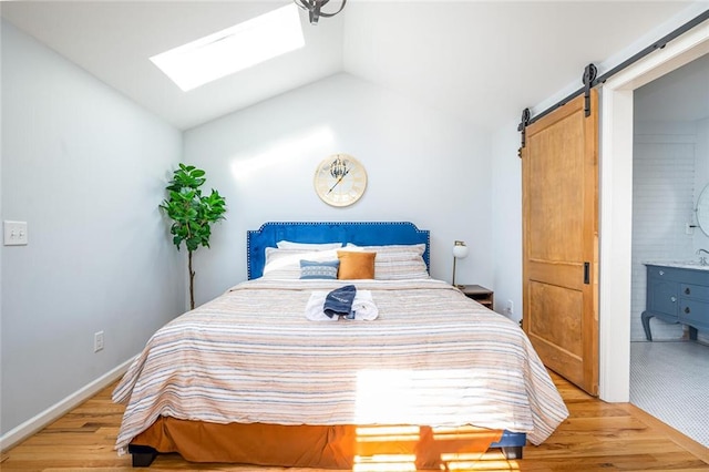 bedroom with baseboards, ensuite bath, vaulted ceiling with skylight, a barn door, and light wood-type flooring