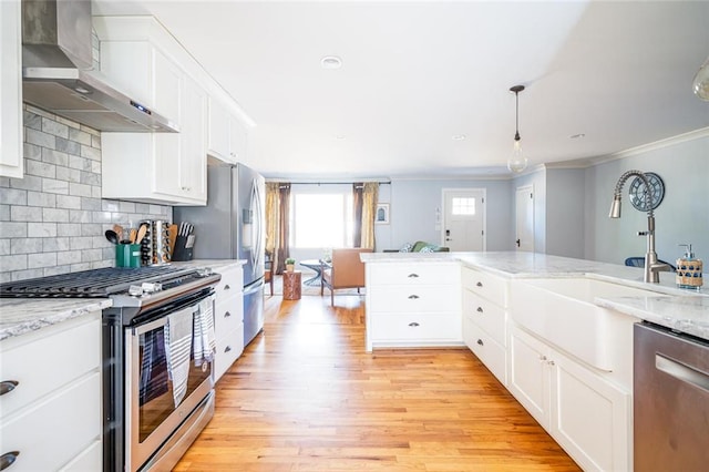 kitchen featuring light wood-style floors, appliances with stainless steel finishes, crown molding, wall chimney exhaust hood, and backsplash