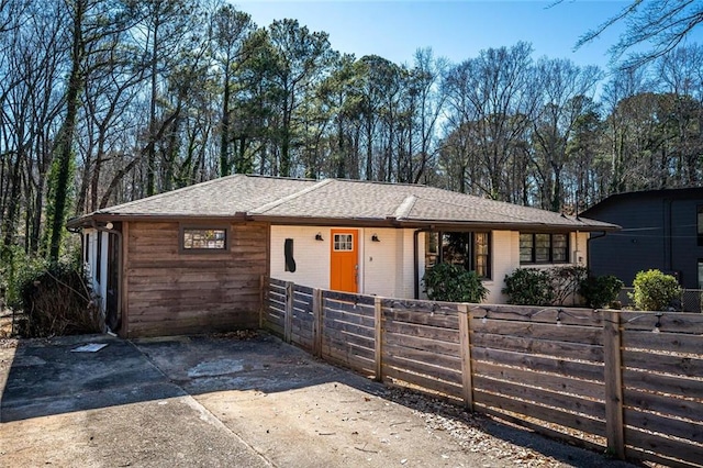 ranch-style house featuring a fenced front yard, a shingled roof, and brick siding