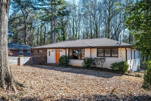 ranch-style house featuring brick siding, roof with shingles, and fence