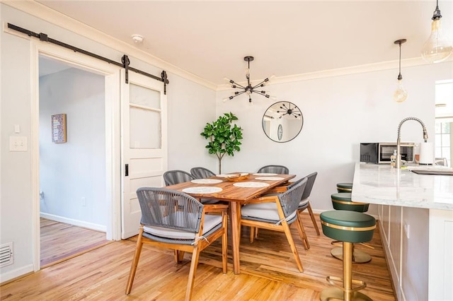 dining room with baseboards, crown molding, a barn door, a notable chandelier, and light wood-type flooring