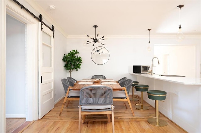 dining room with a barn door, baseboards, light wood-style flooring, and crown molding