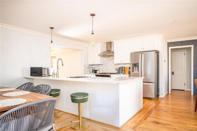 kitchen featuring tasteful backsplash, white cabinetry, stainless steel appliances, wall chimney exhaust hood, and light wood finished floors