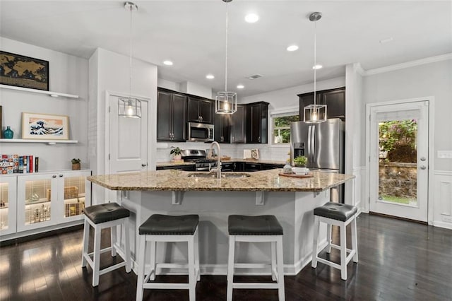 kitchen featuring stainless steel appliances, a sink, decorative backsplash, a center island with sink, and light stone countertops