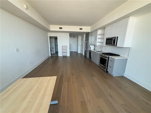 kitchen with tasteful backsplash, sink, stainless steel appliances, white cabinets, and hardwood / wood-style flooring