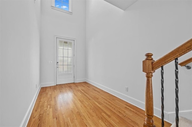 entryway featuring baseboards, light wood-style flooring, and a towering ceiling