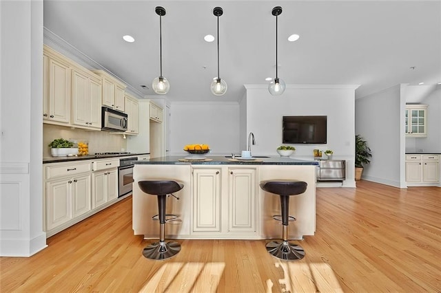 kitchen featuring ornamental molding, dark countertops, cream cabinetry, a sink, and stainless steel appliances