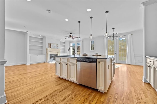 kitchen with stainless steel dishwasher, open floor plan, light wood-type flooring, cream cabinetry, and a sink