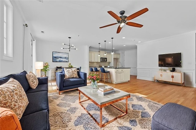 living area featuring crown molding, wainscoting, light wood-type flooring, ceiling fan with notable chandelier, and recessed lighting