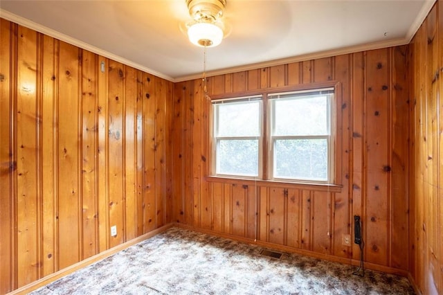 carpeted spare room featuring wood walls, crown molding, a wealth of natural light, and ceiling fan