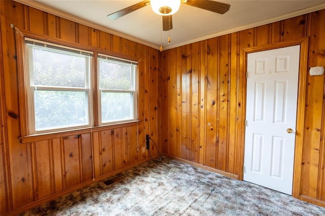 unfurnished room with ornamental molding, wooden walls, carpet floors, and ceiling fan