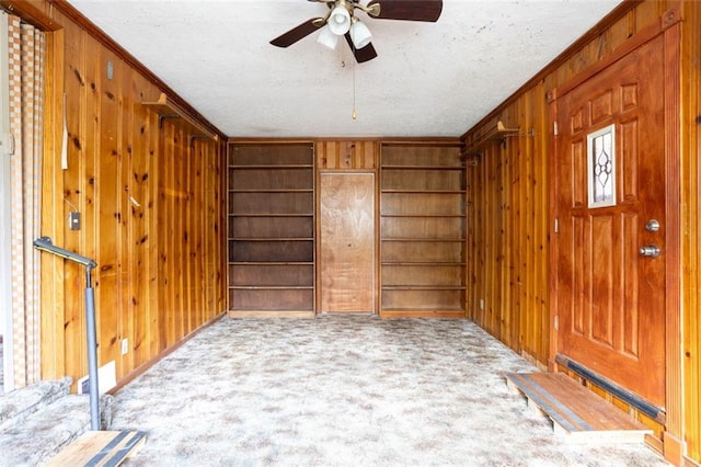 carpeted entryway with wooden walls, ornamental molding, and ceiling fan