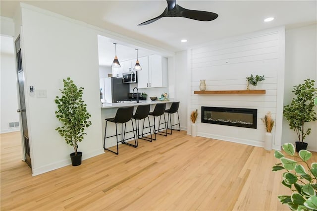 kitchen featuring a breakfast bar area, kitchen peninsula, white cabinetry, and light wood-type flooring