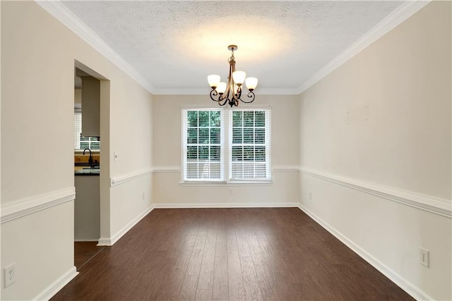 unfurnished dining area with a chandelier, dark wood-style floors, a textured ceiling, baseboards, and ornamental molding