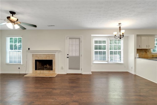 unfurnished living room with dark wood finished floors, a chandelier, a ceiling fan, a tiled fireplace, and a textured ceiling