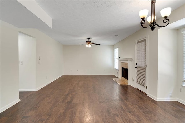 unfurnished living room with ceiling fan, a fireplace, dark wood-type flooring, a chandelier, and baseboards