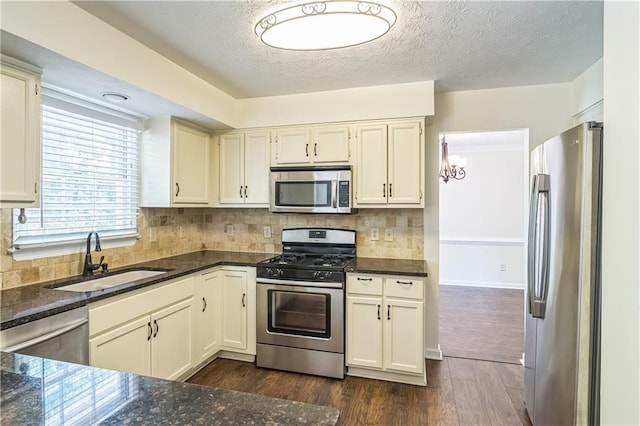 kitchen featuring stainless steel appliances, a sink, dark stone countertops, dark wood finished floors, and decorative backsplash