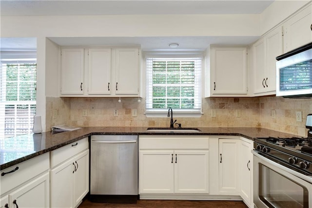kitchen featuring appliances with stainless steel finishes, a sink, dark stone counters, and white cabinets