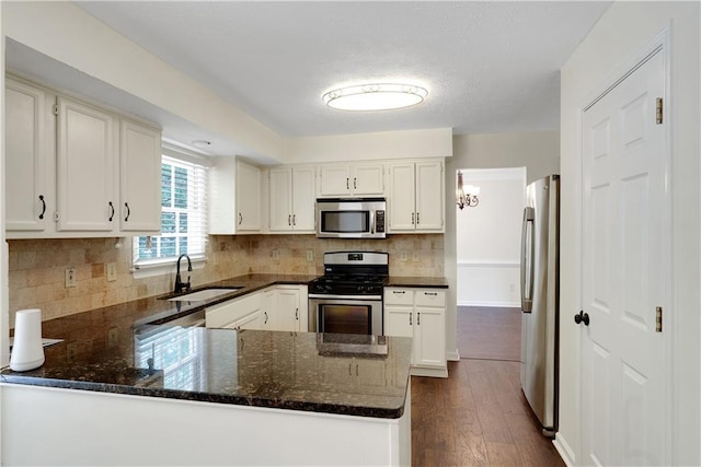 kitchen with appliances with stainless steel finishes, a sink, a peninsula, dark wood-style floors, and dark stone counters