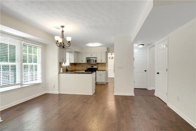 kitchen featuring appliances with stainless steel finishes, a chandelier, dark wood-type flooring, dark countertops, and baseboards