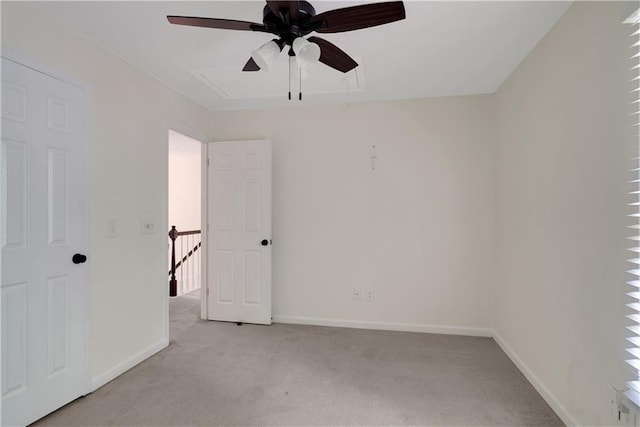 spare room featuring attic access, light colored carpet, a ceiling fan, and baseboards