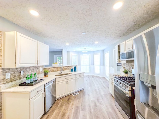 kitchen featuring white cabinetry, a textured ceiling, light wood-type flooring, sink, and stainless steel appliances