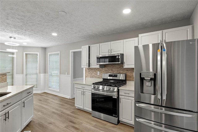 kitchen featuring a textured ceiling, white cabinets, stainless steel appliances, and light wood-type flooring