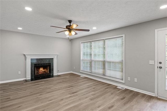 unfurnished living room featuring a premium fireplace, a textured ceiling, light wood-type flooring, and ceiling fan