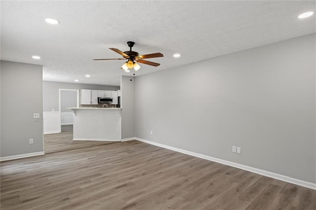 unfurnished living room with a textured ceiling, hardwood / wood-style flooring, and ceiling fan