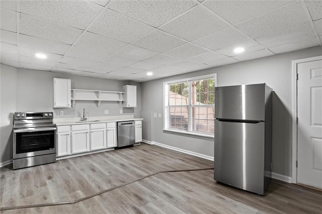 kitchen with appliances with stainless steel finishes, sink, light wood-type flooring, a paneled ceiling, and white cabinets