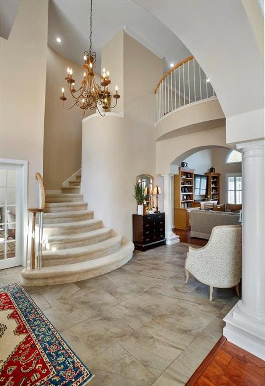 entrance foyer with ornate columns, a towering ceiling, arched walkways, stairway, and a chandelier