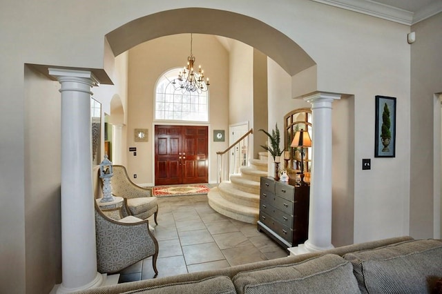 tiled foyer featuring arched walkways, a towering ceiling, decorative columns, a chandelier, and ornamental molding