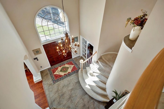 entrance foyer with arched walkways, a towering ceiling, stairs, baseboards, and a chandelier