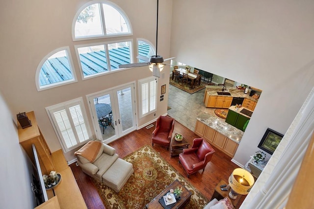 living room with a towering ceiling, plenty of natural light, wood finished floors, ceiling fan, and french doors