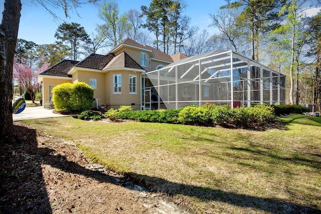 rear view of property with stucco siding, a yard, and glass enclosure