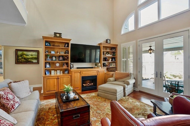 living room with a high ceiling, light wood-style flooring, french doors, a fireplace, and baseboards