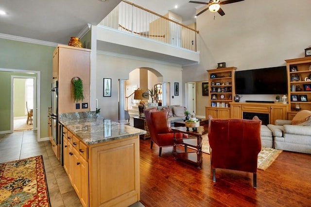 living area with arched walkways, a ceiling fan, decorative columns, a high ceiling, and ornamental molding