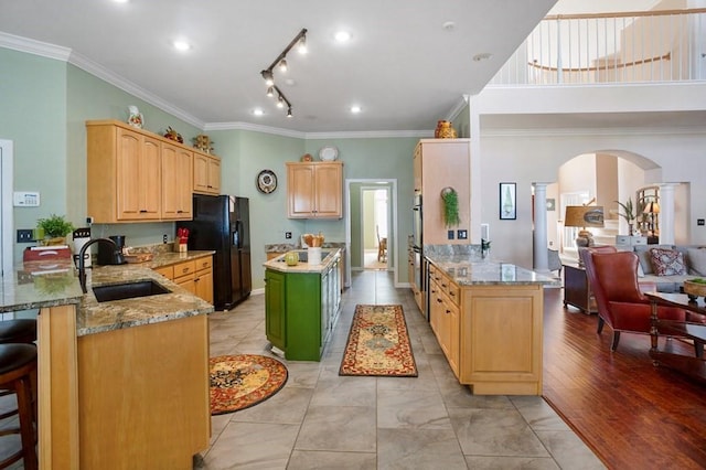kitchen with a sink, a peninsula, black fridge, arched walkways, and ornamental molding