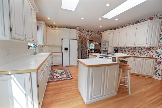 kitchen featuring white appliances, a skylight, white cabinetry, and a kitchen island