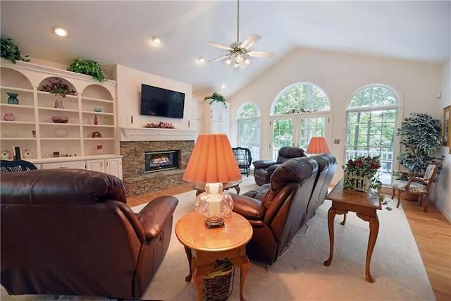 living room featuring lofted ceiling, ceiling fan, a stone fireplace, and light wood-type flooring