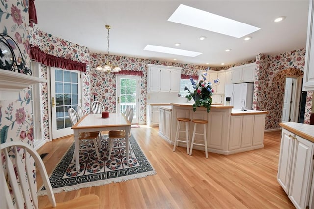 kitchen with a skylight, white cabinetry, white fridge with ice dispenser, light hardwood / wood-style floors, and a center island with sink