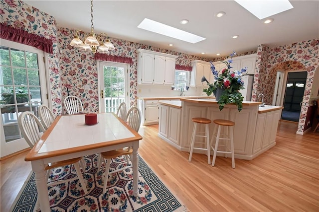 dining area with a notable chandelier, plenty of natural light, a skylight, and light hardwood / wood-style flooring