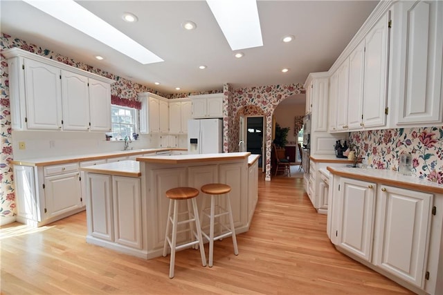 kitchen featuring a skylight, a kitchen island, white refrigerator with ice dispenser, a kitchen bar, and white cabinets