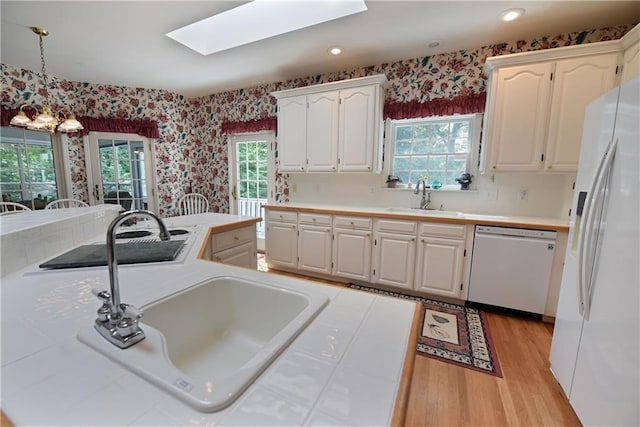 kitchen with a skylight, white cabinetry, sink, and white appliances