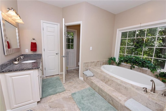 bathroom with tiled tub, vanity, and toilet