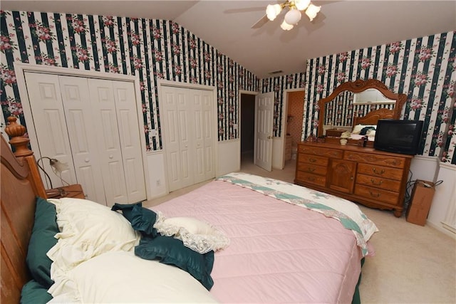 bedroom with two closets, light colored carpet, ceiling fan, and lofted ceiling