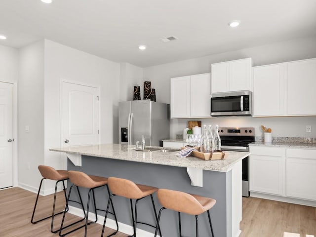 414 Oak View Ln, Dallas, GA 30157 - kitchen with stainless steel appliances, a center island with sink, light wood finished floors, a breakfast bar area, and white cabinets