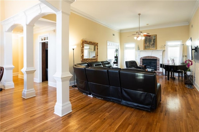 living area with a fireplace, crown molding, ceiling fan, decorative columns, and wood finished floors