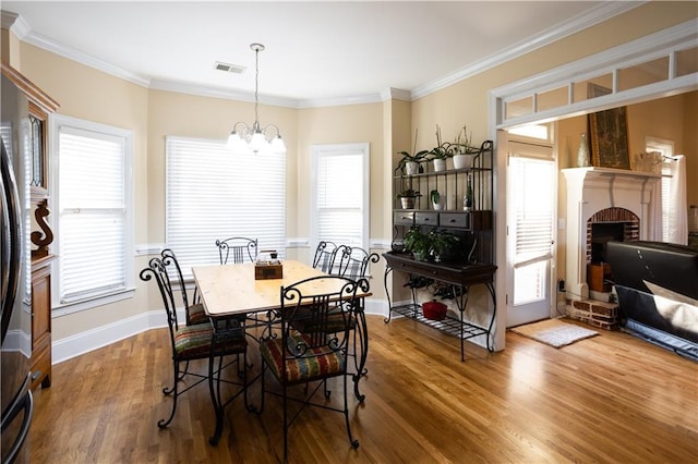 dining area with a fireplace, hardwood / wood-style flooring, a chandelier, and ornamental molding